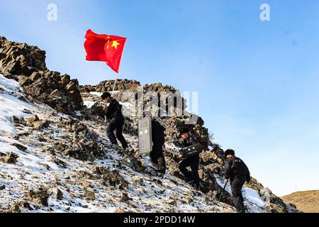 ALTAY, CHINA - MARCH 14, 2023 - Police officers hold national flags as they patrol the border over a snowy mountain in Altay, Xinjiang province, China Stock Photo