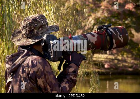 Tokyo, Japan - November 23, 2020: A photographer with its gear takes pictures of migrating birds near the pond in Shinjuku Gyoen Park Stock Photo