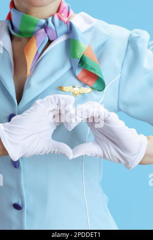 Closeup on female stewardess on blue background in blue uniform showing heart shaped hands. Stock Photo