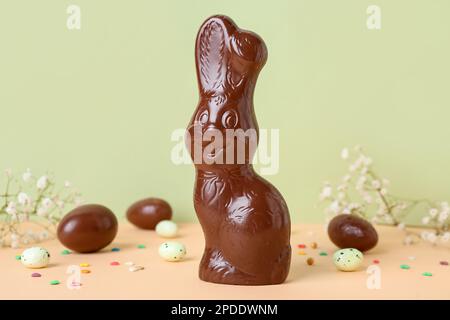 Chocolate Easter bunny with eggs and flowers on table against green background Stock Photo