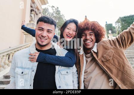 Group of three multiracial young friends having fun and smiling looking at camera. Front view of happy multiethnic people with cheerful attitude. Life style concept. High quality photo Stock Photo