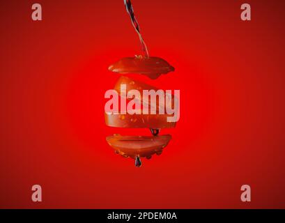 Sliced tomato suspended in the air on a red gradient background with water splashed over it. Stock Photo