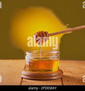 Honey being pored from a drizzling stick in to a glass jar shot on a wooden table. Stock Photo