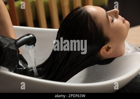 Hairdresser rinsing out dye from woman's hair in beauty salon Stock Photo