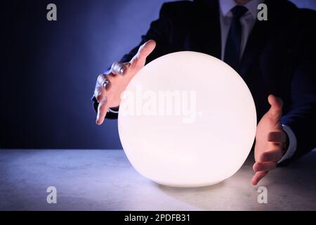 Businessman using glowing crystal ball to predict future at table, closeup. Fortune telling Stock Photo