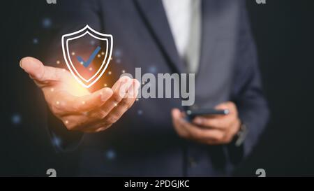 Businessman holding shield protective icon. Smartphone network security protection and data security concept, cyber security and hazard protection. Stock Photo