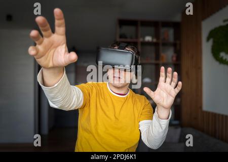 Young caucasian man using virtual reality glasses at home. People and technology metaverse concept. Stock Photo