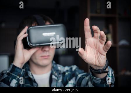 Young caucasian man using virtual reality glasses at home. People and technology metaverse concept. Stock Photo