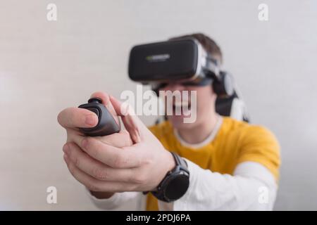 Young man trying virtual reality at home, using headset VR glasses and holding joystick, playing video games. Modern technologies and domestic enterta Stock Photo