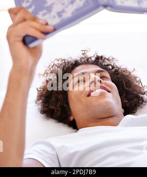 Lazy morning reading. Close-up shot of a handsome young man lying down on his back and holding a book. Stock Photo