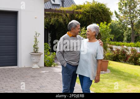 Loving biracial senior couple looking at each other and smiling while standing in yard Stock Photo