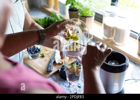 Midsection of biracial senior couple putting fruit slices in mixer while making smoothie in kitchen Stock Photo