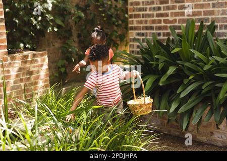 Happy african american children playing egg hunt in garden at easter Stock Photo