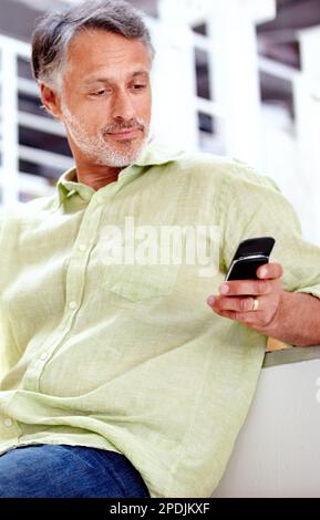 Texting in the workplace. A mature businessman using his cellphone while sitting in the office. Stock Photo