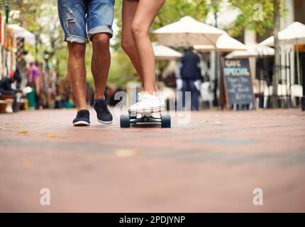 Taking it one ride at a time...a young couples legs with one balancing on a skateboard,. Stock Photo