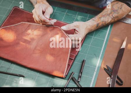 closeup hand working process leather handcraft in the leather workshop. Man holding crafting tool and working. He is sewing hammer to make a walet. Ta Stock Photo