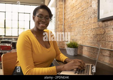 portrait african black woman office employee sitting in modern office using laptop computer happy smiling Stock Photo