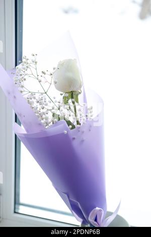 bouquet of white roses in purple packaging on the windowsill Stock Photo