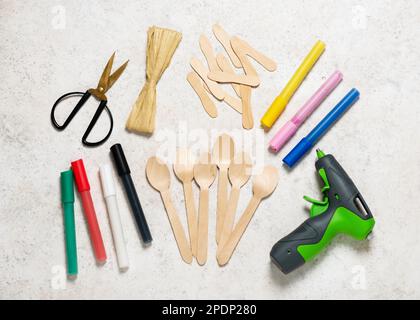 Top view of craft workplace with wooden spoons and ice cream spades, glue gun, scissors, acrylic painter, paper raffia for making cute easter bunny Stock Photo