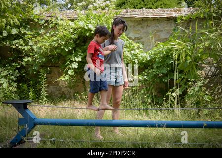young boy walking on a wire with the help of a woman coach in a garden Stock Photo