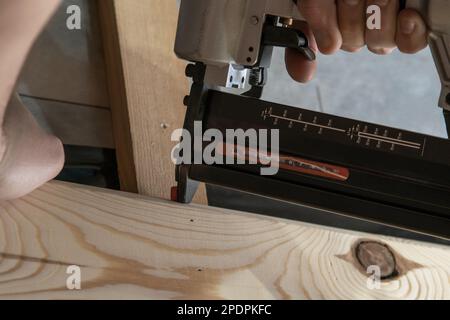 Cropped man hands using pneumatic construction stapler, pistol nail gun for wooden plank. Clipping, scoring metal nails and staples. Hammer Stock Photo