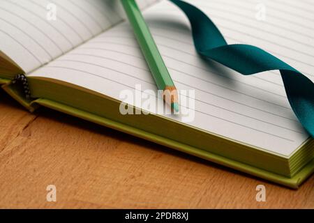 A lined notebook with a green pencil. Ready to take notes, sketch ideas and write plans. Pencil and paper at the ready. Stock Photo