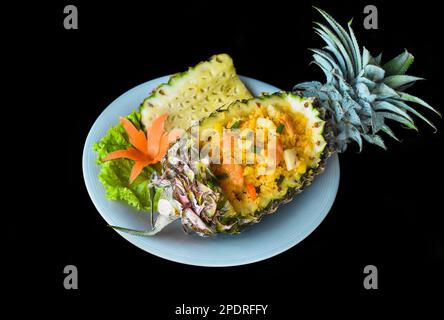 Fried rice with seafood in a pineapple with vegetables on blue plate isolated on black background top view Stock Photo