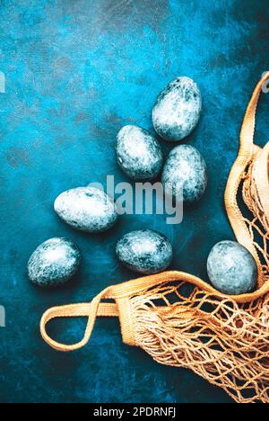 Easter composition with blue painted eggs in an eco-friendly shopping bag on blue background, top view Stock Photo