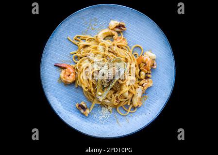 Pasta carbonara with seafood on blue plate  with shrimps isolated on black background top view Stock Photo