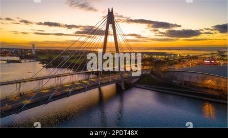 An aerial view of a bridge over a body of water at dusk with sunset in the background Stock Photo