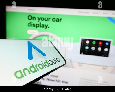 Cellphone with logo of mobile app Android Auto (Google) on screen in front of website. Focus on center-right of phone display. Stock Photo