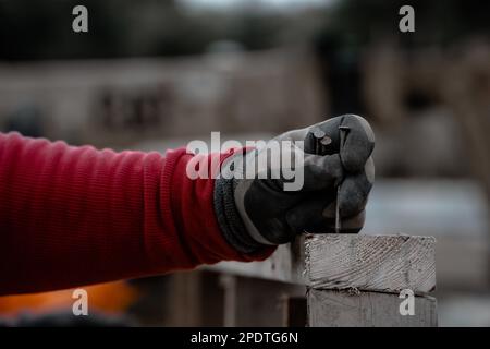A close-up shot of a construction worker holding a nail to fix it on a wood piece Stock Photo