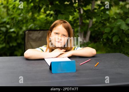 Online remote learning. School kids with phone having video conference chat with teacher and class group. Child learns in the garden .Looks into the camera. Front view Stock Photo
