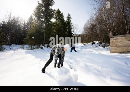 Two happy boys together sculpt snow globe for snowman. Brothers game outdoor in winter with snow in mountains. Stock Photo