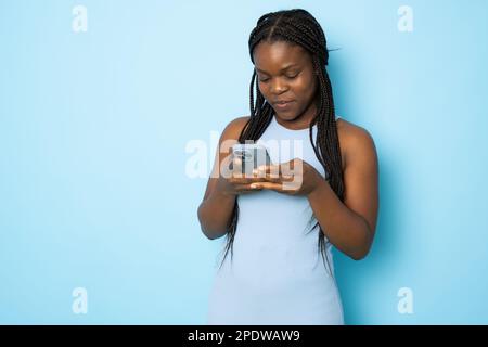 Portrait of young cheerful black lady using Smartphone For Messaging With Friends, Happy African American Lady Texting On Cellphone while standing Ove Stock Photo