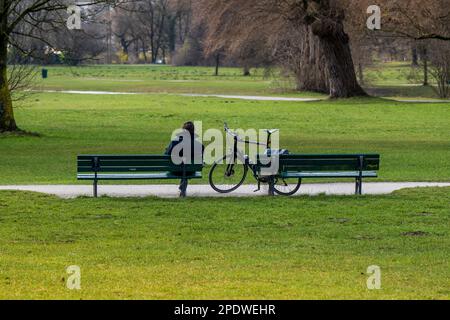 Munich, Germany. 15th Mar, 2023. A woman sits on a park bench in the English Garden in the sun. Credit: Peter Kneffel/dpa/Alamy Live News Stock Photo