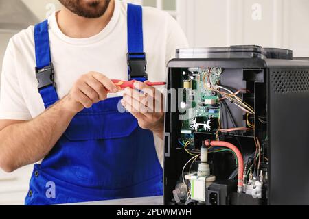 Repairman with screwdriver fixing coffee machine indoors, closeup Stock Photo