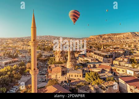 Aerial view of mosque minaret and hot air balloons among hotels and houses carved into volcanic tuff in Cappadocia - one of the wonders of Turkey. Stock Photo