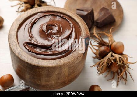 Bowl of tasty chocolate paste with hazelnuts on white wooden table Stock Photo