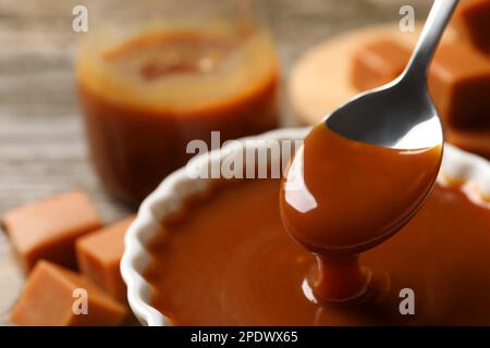 Taking tasty salted caramel with spoon from bowl at table, closeup Stock Photo