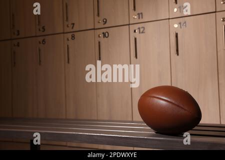 Leather American football ball on wooden bench in locker room. Space for text Stock Photo