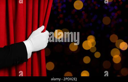 Man opening red front curtain against blurred lights. Bokeh effect Stock Photo