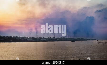 A blanket of polluted smog from belching chimneys at brick kilns on the Mekong River at Long Xuyen in An Giang Province, Vietnam. Stock Photo