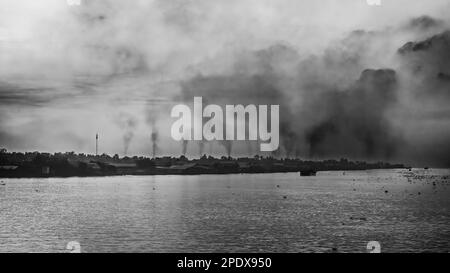 A blanket of polluted smog from belching chimneys at brick kilns on the Mekong River at Long Xuyen in An Giang Province, Vietnam. Stock Photo