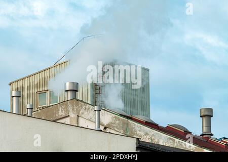 Industrial chimney fume and steam exhaustion on old factory building, selective focus Stock Photo
