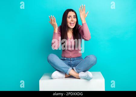 Photo of offended dissatisfied girl straight hairdo pastel cardigan sitting on cube complains isolated on vibrant teal color background Stock Photo