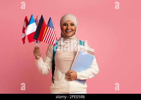 Portrait Of Smiling Muslim Female Student Holding International Flags And Workbooks Stock Photo