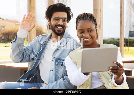 Smiling young black and arabic people students studying with tablet together, have meeting, waving hand Stock Photo
