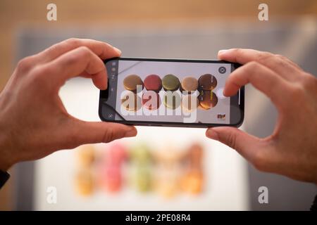Male hands holding smartphone with broken screen, taking macarons photo Stock Photo