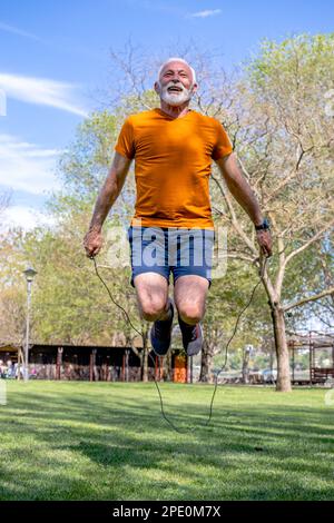 Active senior male jumping the rope. Determined elderly man exercising in the park. Skipping rope. Stock Photo
